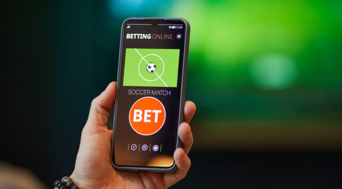 Close-up of hand holding smartphone with soccer betting app interface showing bet options and match information in background