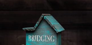 Bridging Loans in the UK: The Fastest Way to Solve Short-Term Cash Flow Problems Wooden house model with coins next to it with conceptual text. Bridging loan