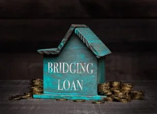 Wooden house model with coins next to it with conceptual text. Bridging loan
