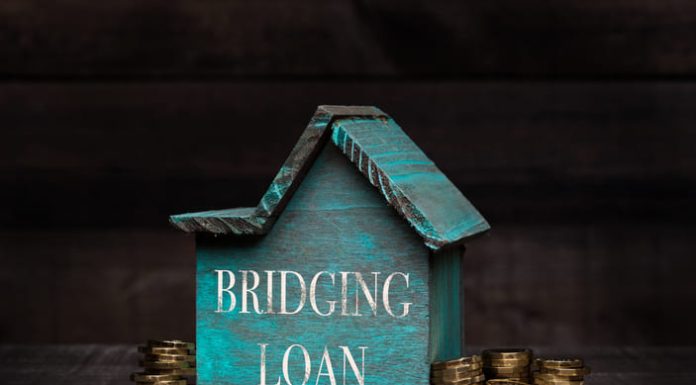 Wooden house model with coins next to it with conceptual text. Bridging loan