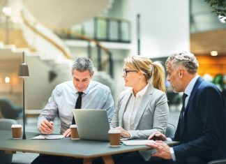 Mature businesspeople sitting at a table talking and using a laptop while having a meeting together about entrepreneurship