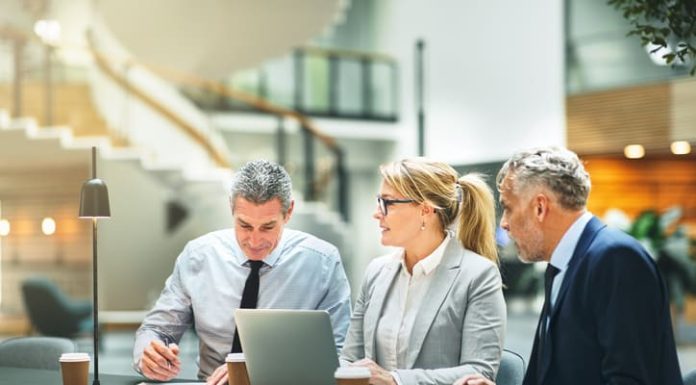 Mature businesspeople sitting at a table talking and using a laptop while having a meeting together about entrepreneurship