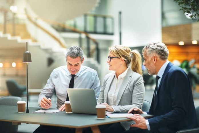 iStock-947363918 (1) Mature businesspeople sitting at a table talking and using a laptop while having a meeting together about entrepreneurship