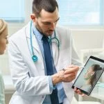 Plastic / Cosmetic Surgeon Consults Woman about Facial Lift Surgery, He Draws Arrows on Digital Tablet Computer Screen, Showing Types of Facelift, Forehead Correcting Procedures Available for Her.