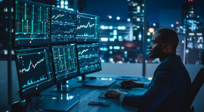 Financial Analyst Working on Computer with Multi-Monitor Workstation with Real-Time Stocks and trading, Commodities and Exchange Market Charts.