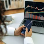 Investment, trading in the stock market. The girl uses a phone and a laptop, looks through the stock market, analyzes stocks, a stock trader assesses risks and possible profits, develops a strategy