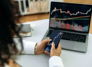 Investment, trading in the stock market. The girl uses a phone and a laptop, looks through the stock market, analyzes stocks, a stock trader assesses risks and possible profits, develops a strategy