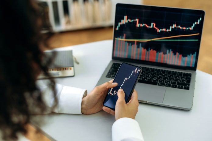 Investment, trading in the stock market. The girl uses a phone and a laptop, looks through the stock market, analyzes stocks, a stock trader assesses risks and possible profits, develops a strategy