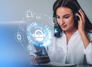Businesswoman in headphones is holding smartphone with digital interface with various holograms having online conference call. Robot, smart watch, pie diagram. Office workplace with laptop, notebook