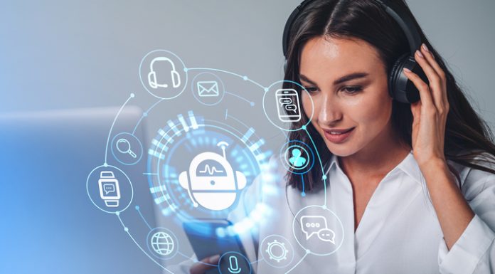 Businesswoman in headphones is holding smartphone with digital interface with various holograms having online conference call. Robot, smart watch, pie diagram. Office workplace with laptop, notebook