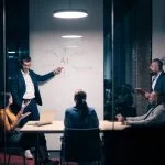 Chief AI Officer with diverse business team in modern office during a late-night meeting. Professional discussion on artificial intelligence strategy. Concept of corporate teamwork, innovation, and AI technology.