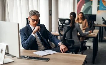 A business leader shifting his focus at his desk in a vibrant office, illustrating productivity and teamwork.