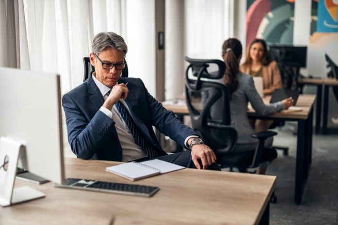 A business leader shifting his focus at his desk in a vibrant office, illustrating productivity and teamwork.