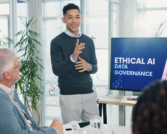 Gartner: The Leadership Blind Spot: Why Executive AI Literacy Will Shape Business Outcomes in 2025 Man, presentation and screen with meeting for AI ethics, smile and planning for future web development at office. Person, speaker and staff in boardroom with data governance at startup tech agency