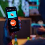 online sports betting app, Angliabet with football match bet option visible on screen, sitting indoors.