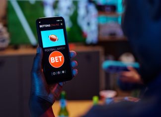 online sports betting app, Angliabet with football match bet option visible on screen, sitting indoors.