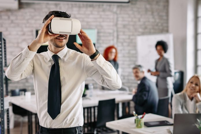 Young businessman using virtual reality headset while working in the office. Businessman wearing VR glasses and having fun at work.