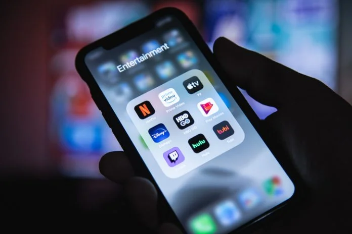 Apple XS Smartphone in Hand with Group of Streaming Applications Netflix Buys Warner Bros. Discovery