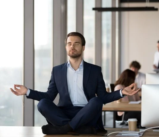 Calm businessman in suit meditating on office desk for Spiritual Awareness