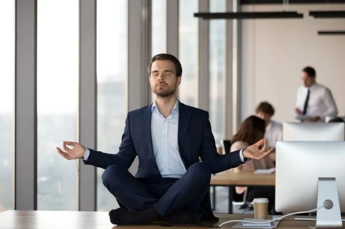 Calm businessman in suit meditating on office desk for Spiritual Awareness