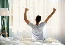 Guy sitting on bed facing the window, awakening after good sleep and rest prioritizing self-care