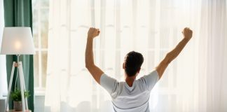 The Power of Self-Care in Boosting Your Productivity Guy sitting on bed facing the window, awakening after good sleep and rest prioritizing self-care