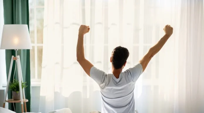 The Power of Self-Care in Boosting Your Productivity Guy sitting on bed facing the window, awakening after good sleep and rest prioritizing self-care