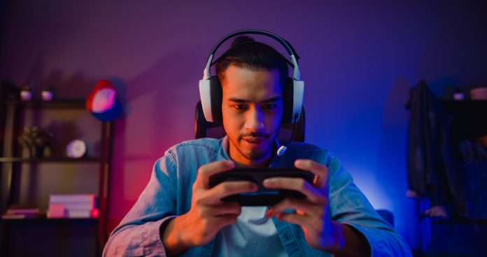 Happy asia man gamer wear headphone competition play video game online with smartphone colorful neon light in living room at night modern house. How to Promote a Mobile Game