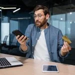 The Sweet Trap: A Man’s Guide to Dodging Sugar Baby Scams Frustrated and deceived businessman in office trying to make purchase in online store and online money transfer from bank credit card, annoyed man working inside office using laptop and phone. Sugar baby scam online