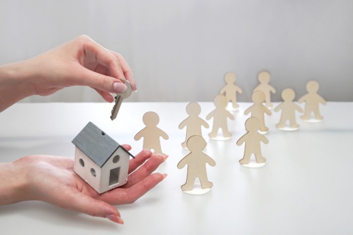Hand holding a model of a house and a key, offering it to figures of people Hand holding a model of a house and a key, offering it to figures of people. Supportive housing concept