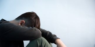 Why Mental Health Is Suffering in the UK Person sitting in low light holding their legs, symbolizing stress and anxiety caused by the cost of living and the growing mental health crisis in the UK.