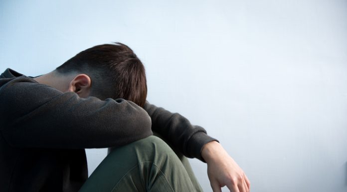 Why Mental Health Is Suffering in the UK Person sitting in low light holding their legs, symbolizing stress and anxiety caused by the cost of living and the growing mental health crisis in the UK.