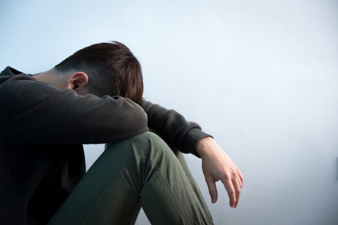 depression man sit on floor Person sitting in low light holding their legs, symbolizing stress and anxiety caused by the cost of living and the growing mental health crisis in the UK.