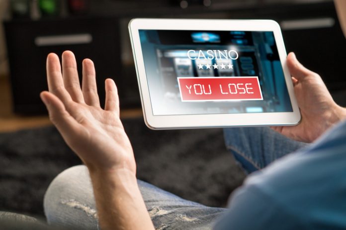 Losing money in online casino. Man playing online slot machine game with tablet. Playing 1xbet in online casino