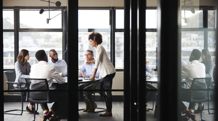 Why Strategy Isn’t Just for CEOs – and How to Implement It Millennial businesswoman stands addressing colleagues and thinking new strategy at a meeting, seen through glass wall