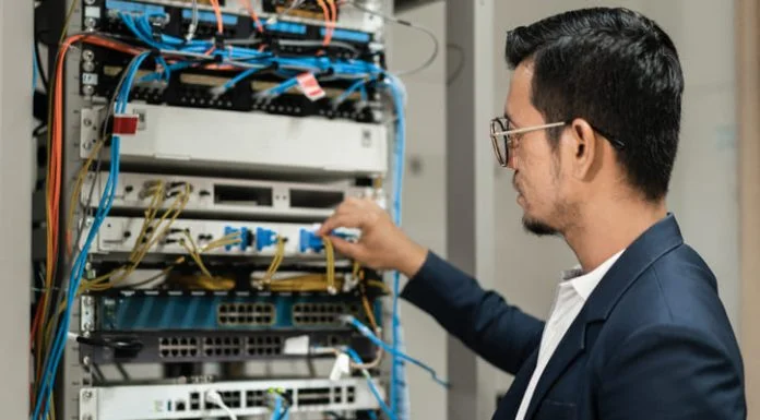 The ROI of Network Infrastructure Modernization Young network technician holding tablet working to connecting network cables in server cabinet in network server room.