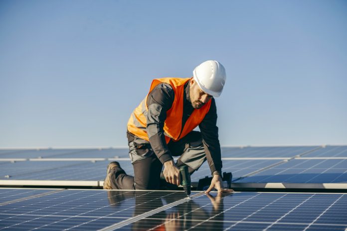 Worker installs solar panels on rooftop. UK Commercial Solar ROI