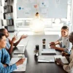 Bright lightbulb hanging from the roof while a group of businesspeople are having a meeting in an office at work.