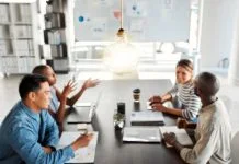 Designed Informality: Reclaiming the Oxygen of Work Bright lightbulb hanging from the roof while a group of businesspeople are having a meeting in an office at work.