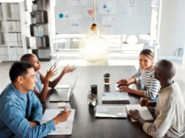Bright lightbulb hanging from the roof while a group of businesspeople are having a meeting in an office at work.