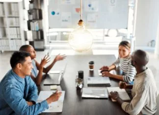 Designed Informality: Reclaiming the Oxygen of Work Bright lightbulb hanging from the roof while a group of businesspeople are having a meeting in an office at work.
