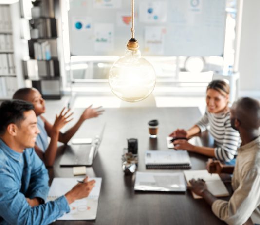 Designed Informality: Reclaiming the Oxygen of Work Bright lightbulb hanging from the roof while a group of businesspeople are having a meeting in an office at work.