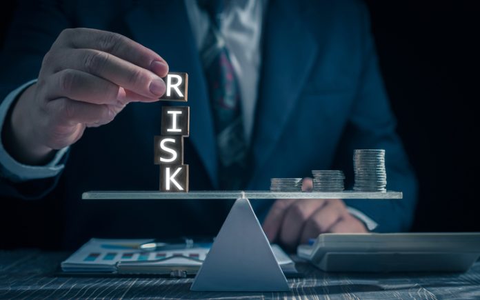 Economic risk management concept. Businessman holding wooden block with word RISK. With level coin balance, banking, financial crisis, bad debt, inflation and interest rates. Investment protection. Aligning Business Insurance With Annual Risk Assessments