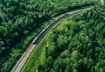 5G train in beautiful green summer forest. Long commuter train moving to rail way station