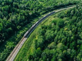 5G train in beautiful green summer forest. Long commuter train moving to rail way station