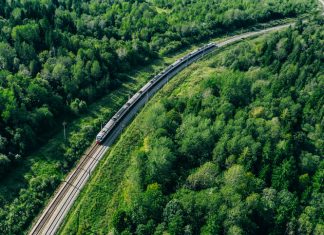 5G train in beautiful green summer forest. Long commuter train moving to rail way station
