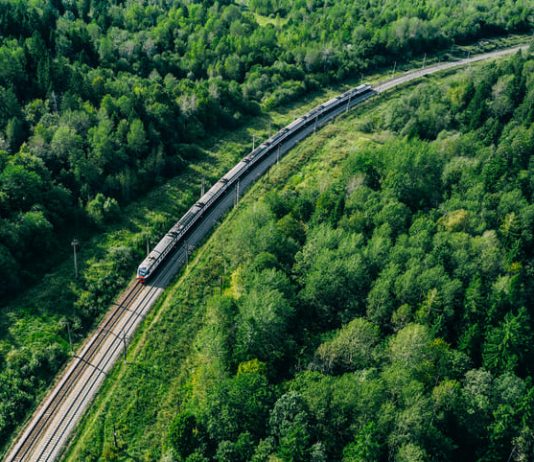 5G train in beautiful green summer forest. Long commuter train moving to rail way station