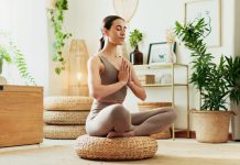 From Burnout to Balance: How Recovery Principles Are Shaping the Future of Workplace Wellness A woman meditating in a bright living room surrounded by indoor plants, practicing mindfulness, wellness and relaxation.
