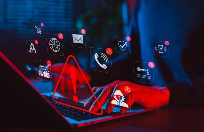 Online scam alert and cybersecurity warning concept. Man holding phone while using laptop, warning sign for scam with icons online threats, phishing, cyber secure, unknown person, suspicious scammer, Account Takeover Fraud in 2026