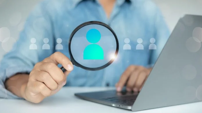 A man holding a magnifying glass focuses on a candidate icon with a laptop, representing recruitment, human resources search, talent acquisition, and the employee selection process. 5 Important Steps for Success in the Executive Search Process